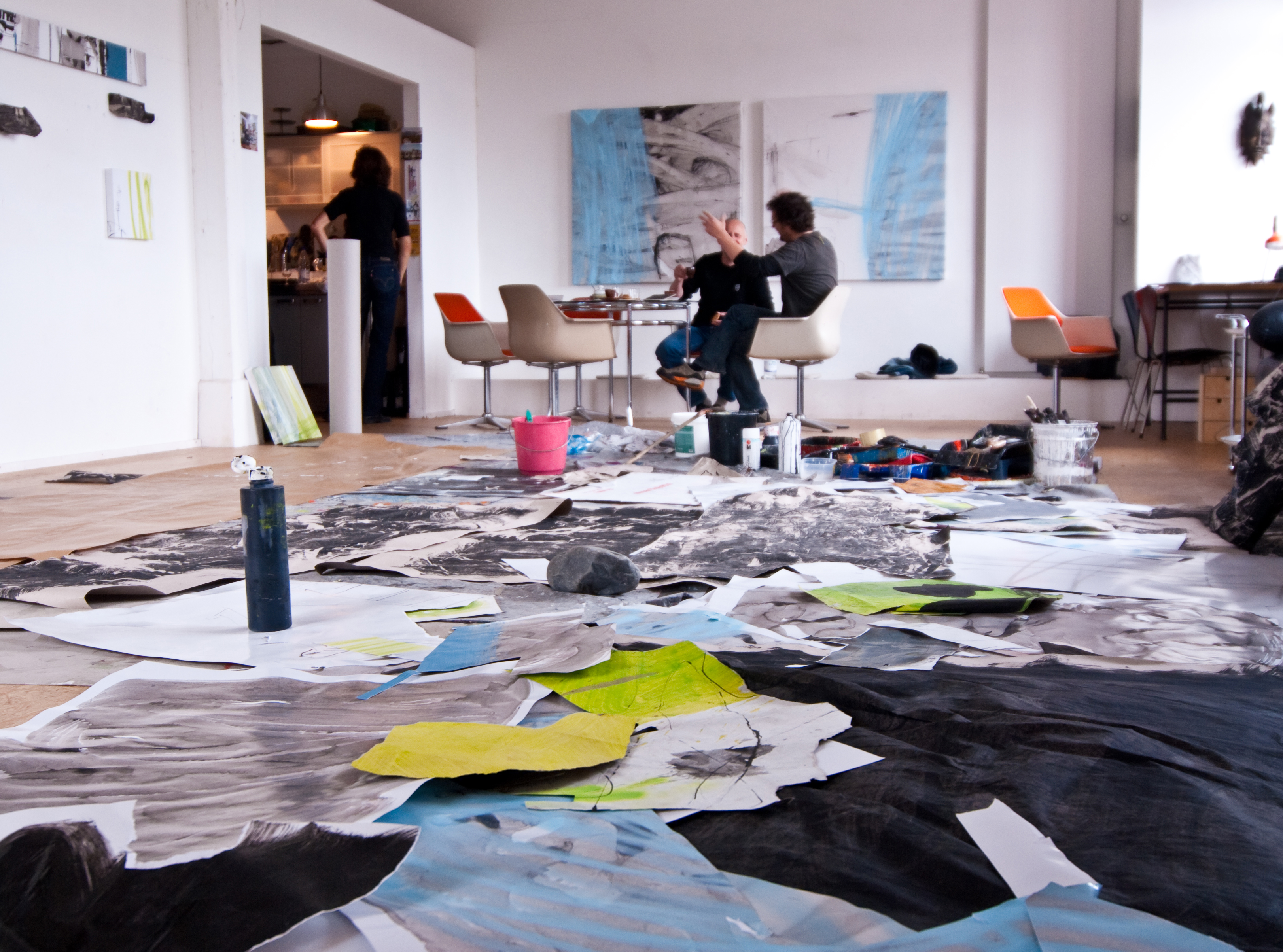 Künstler im Gespräch an der Sitzgruppe des Ateliers, davor großformatige Arbeiten auf dem Boden