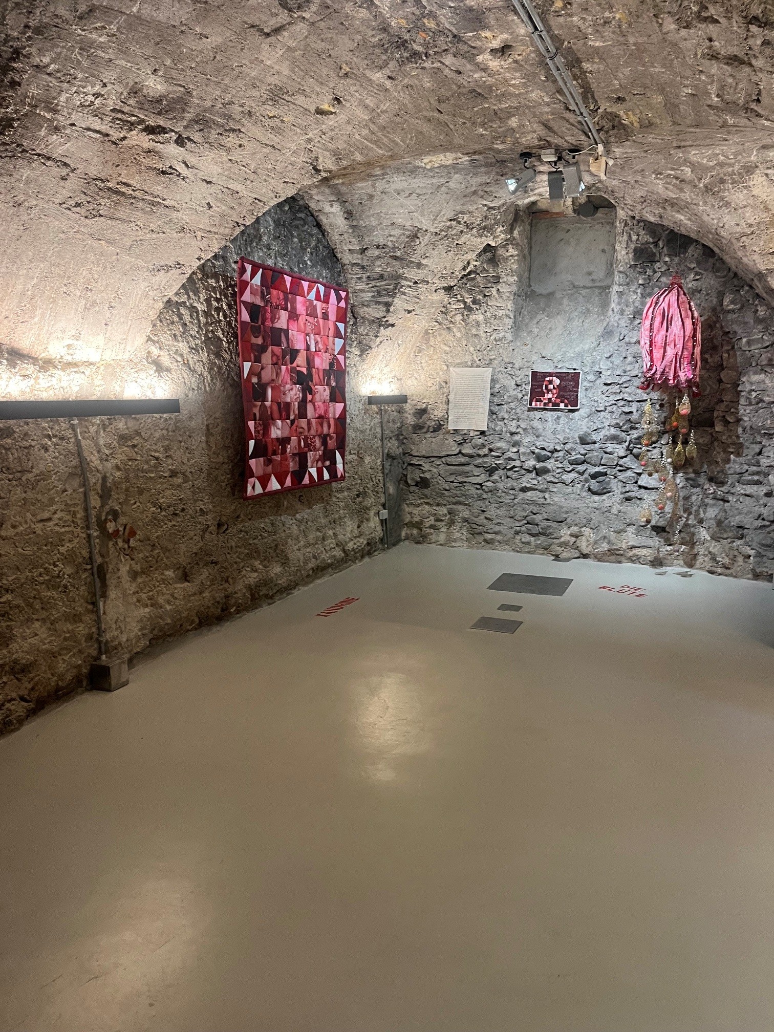 Ausstellungsansicht im Gewölbekeller mit Textilarbeiten an den Natursteinwänden