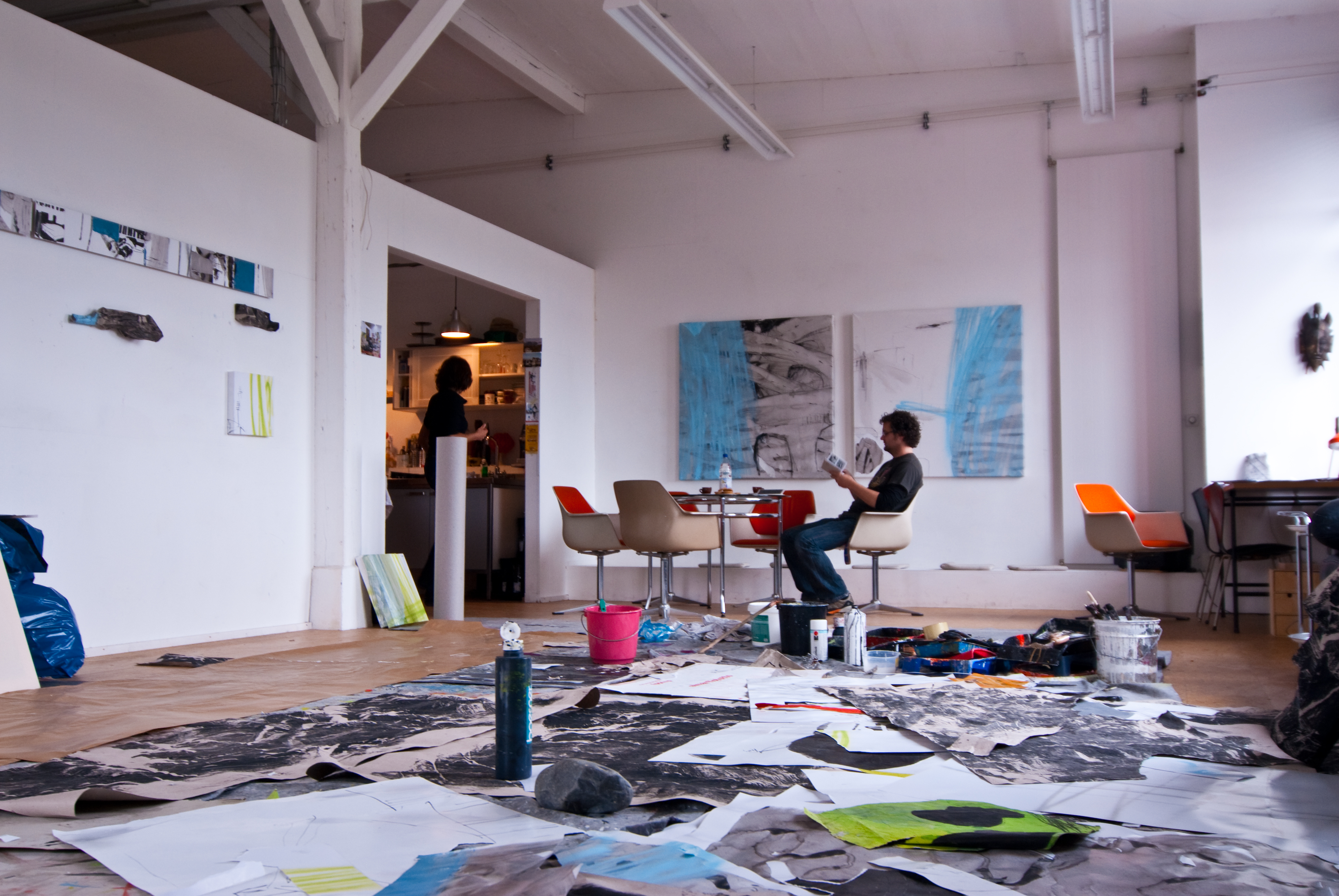 Künstler sitzt lesend im Atelier zwischen großformatigen Malereien und Arbeiten auf dem Boden