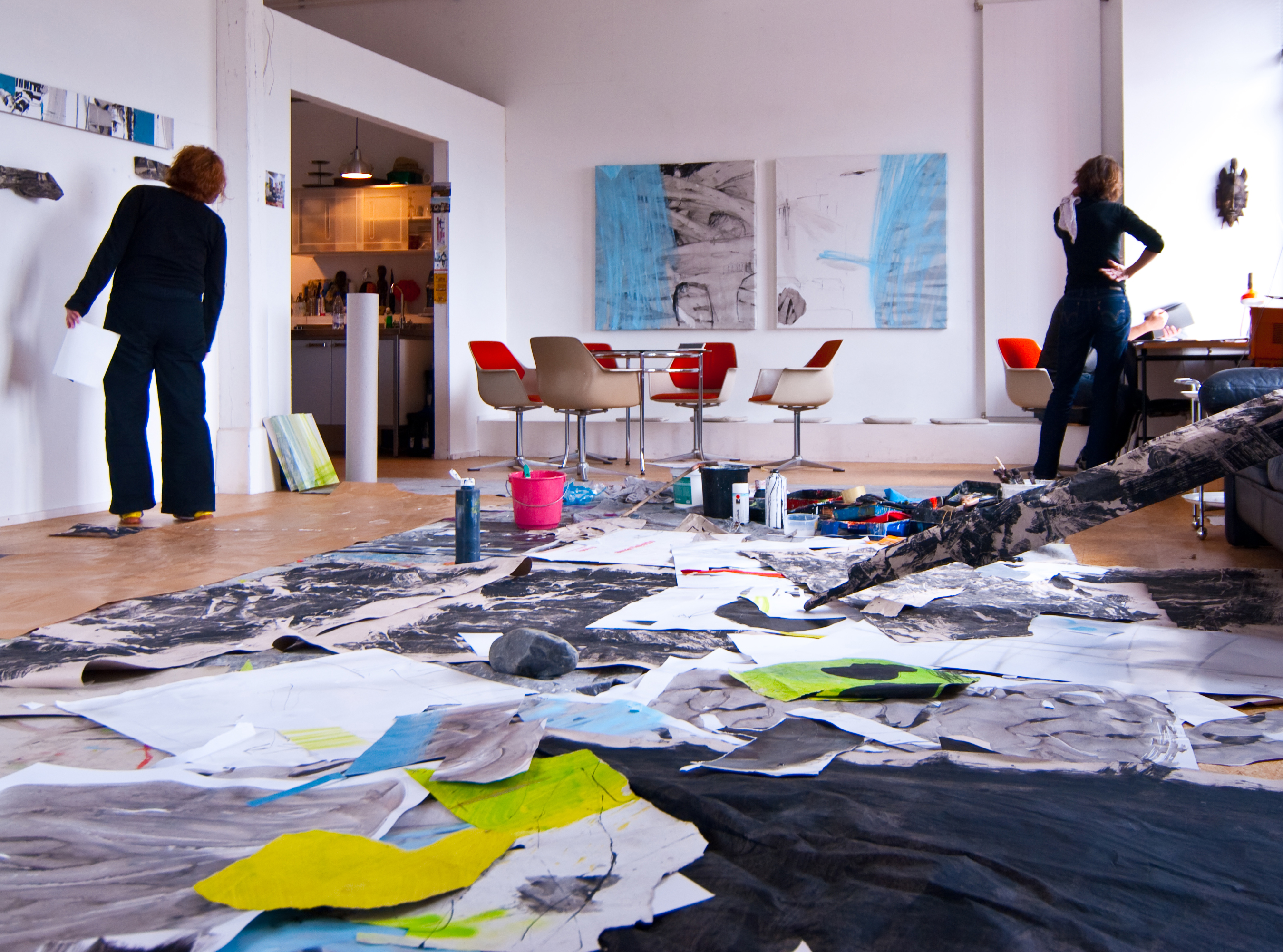 Zwei Künstlerinnen arbeiten in einem hellen Atelier mit großformatigen Arbeiten auf dem Boden