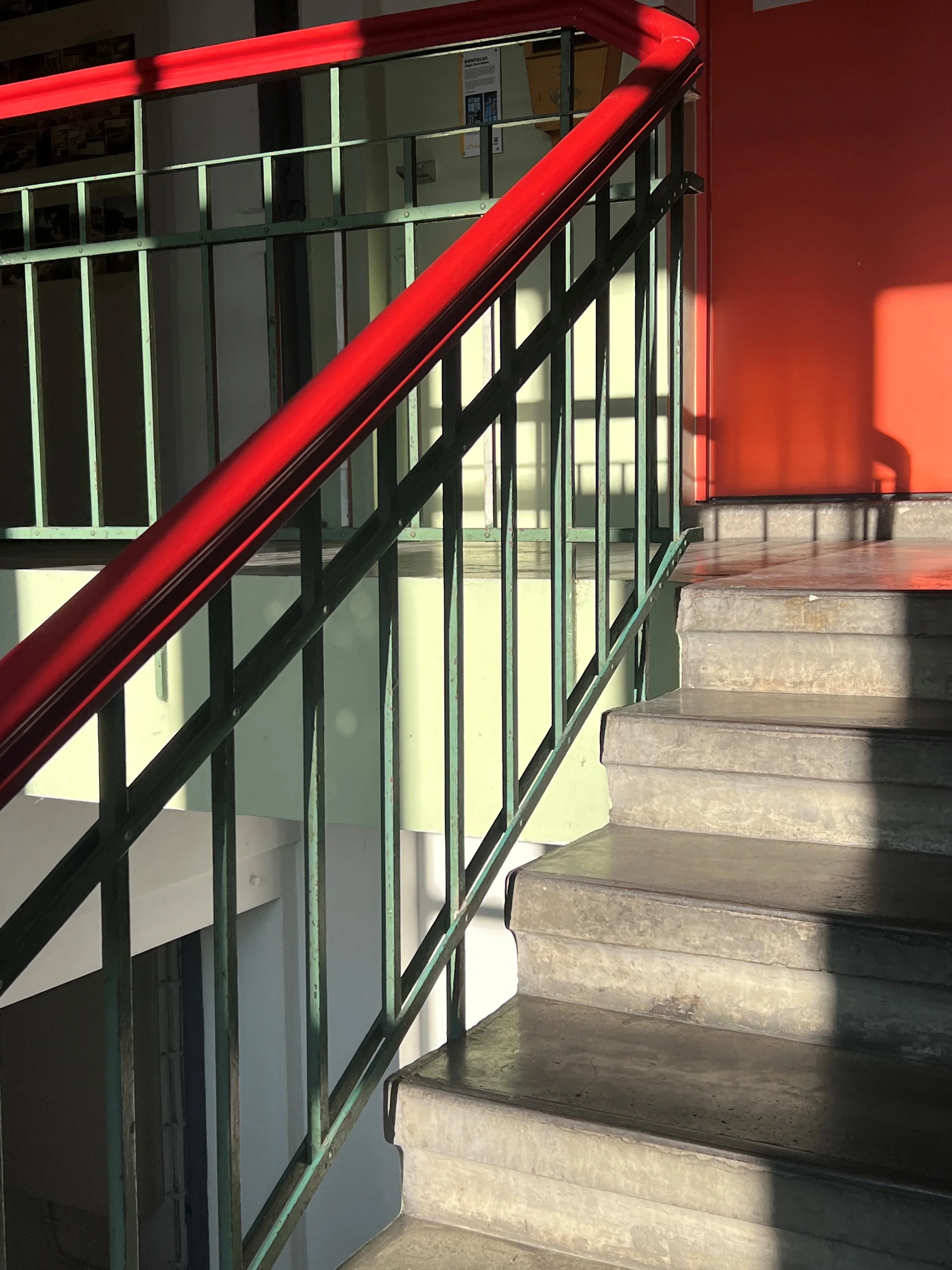 Treppenhaus im Neuwerk mit rotem Handlauf und grünem Geländer im Sonnenlicht