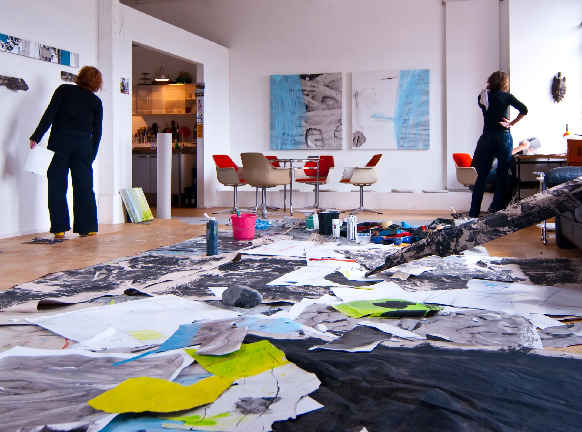 Zwei Künstlerinnen arbeiten in einem hellen Atelier mit großformatigen Arbeiten auf dem Boden